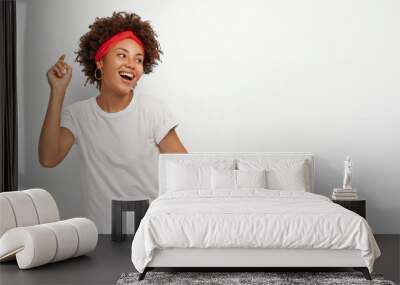 Horizontal shot of happy upbeat African American woman raises arms, looks away with delighted expression, dressed in casual wear, isolated over white background, blank space for your promotion Wall mural