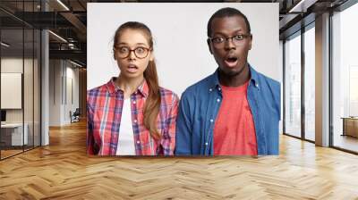 Human facial expressions and emotions. Horizontal studio shot of two surprised astonished young people looking at camera in full disbelief and shock, keeping eyes popped out and jaws dropped Wall mural