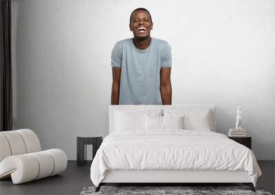 Human feelings and emotions. Body language. Studio shot of young cheerful African male, dressed casually, hands in pockets of yellow pants, shrugging, laughing at camera, isolated on white background Wall mural