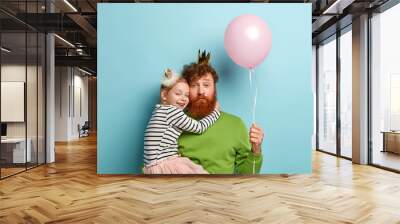 I love you, dad! Bearded redhead father plays with cute little girl, holds balloon, recieves hug from female child, dressed in festive clothes, celebrate Childrens Day together. Family relationships Wall mural