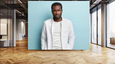 Image of sad sorrowful black man with thick bristle, wears white shirt, feels troublesome, looks at camera with miserable expression, isolated over blue background. People, melancholy, problem concept Wall mural