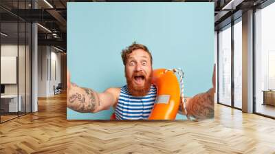 Impressed happy surprised male swimmer shouts at camera, stares with bugged eyes, makes selfie, learns lifesaving skills and how to overcome potential hazards, poses with lifebuoy, stands indoor Wall mural