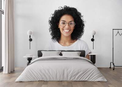 Indoor portrait of beautiful brunette young dark-skinned woman with shaggy hairstyle smiling cheerfully, showing her white teeth to camera while feeling happy and carefree on her first day-off Wall mural