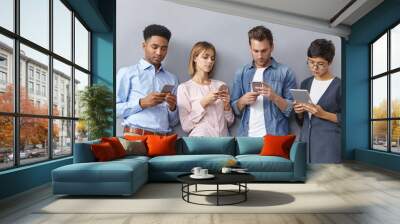 Indoor shot of four people from different nations working together in one company, doing team work, using modern gadgets for preparing presentation, being focused on their work, being always in touch Wall mural