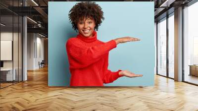 indoor shot of happy woman with dark skin, afro hairstyle, shapes height of object, has appealing lo Wall mural