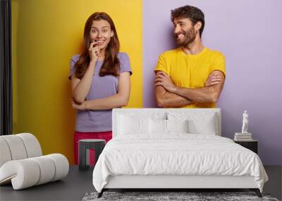 Indoor shot of positive young woman and man smile happily, being in good mood, spend free time together, wear t shirts, pose against purple background. People, relationship and emotions concept Wall mural