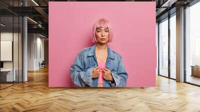 Indoor shot of serious pink haired female model dressed in top and oversized denim jacket, looks directly at camera, wears minimal makeup, isolated over rosy background. Beauty and youth concept Wall mural