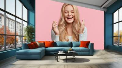 Isolated shot of joyful blonde young cute woman laughs joyfully as hears funny anecdote from friend, has long light hair, poses against pink studio wall. Happiness and positive emotions concept Wall mural