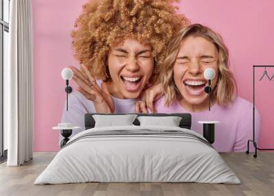 Joyful optimistic young women laugh positively exclaim loudly feels very happy express positive emotions keep eyes shut dressed in casual clothes isolated over pink background. Happiness concept Wall mural