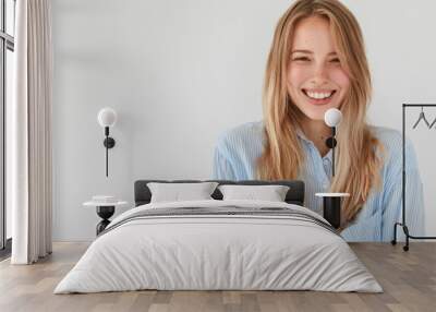 Joyful pretty young woman giggles positively at camera, dressed in casual shirt, shows beauty, poses against white background with blank copy space for your advertisement or promotional text Wall mural