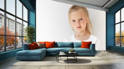 Little blond girl with attractive appearance posing in white background. Natural beauty and morning light suit her pretty and restful facial expression. Wall mural