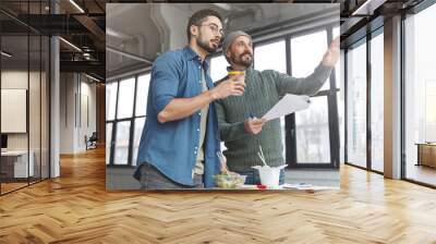 Mature bearded marketing director and his assistant choose place where conduct meeting with business patrners, points at spacious cabinet, have coffee break or lunch, prepare financial report Wall mural