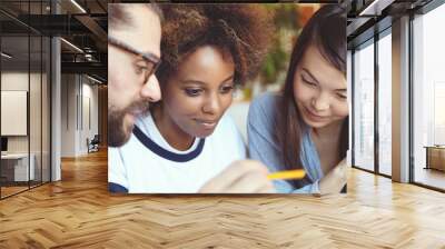 Multiethnic group of young partners discussing their business plans. Handsome man in glasses holding pen, showing his female companions on notebook or pc tablet, explaining his ideas and vision Wall mural