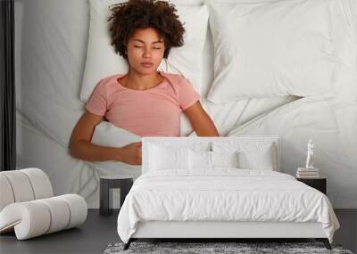 Night time concept. Restful dark skinned curly woman has sleep time, slumber and sweet dreams, poses on white fresh linen, rests after tired day, being in resting state, fell into deep sleep Wall mural