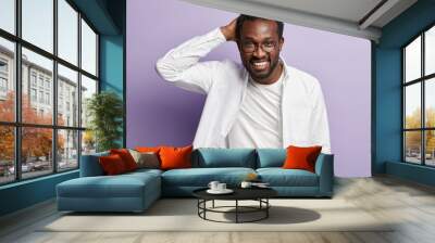 Optimistic glad black male entrepreneur rejoices good results, keeps hands behind head, smiles broadly, dressed in white clothes, isolated over purple background. Ethnicity, happiness, masculinity Wall mural