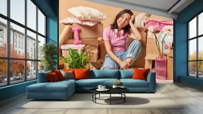 Pensive young Asian woman sits tired on floor thinks about something dressed in casual clothes relocates in new house surrounded by cardboard boxes full of personal belongings going to move in Wall mural