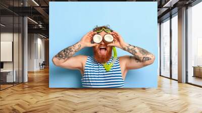 People, summer vacation, snorkeling and swimming concept. Funny bearded ginger man wears snorkel mask, striped sailor t shirt, keeps two coconuts on eyes, looks into distance, has fun at beach Wall mural