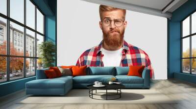 Photo of bewildered puzzled man with thick ginger beard and mustache, raises eyebrows, looks doubtfully at camera, wears fashionable clothes, isolated over white background. Facial expressions Wall mural