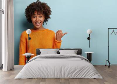 photo of delighted cheerful afro american woman with crisp hair, points away, shows blank space, hap Wall mural