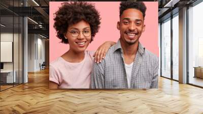 Photo of friendly African American male and female stand close to each other, have broad smiles on faces, have date together, pose against pink background. Beautiful dark skinned woman and her friend Wall mural