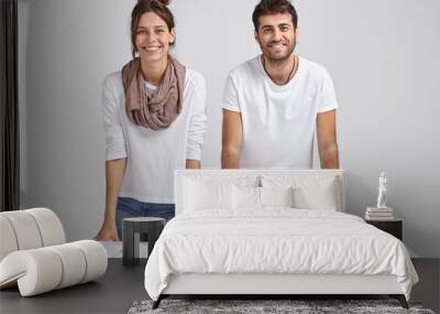 Photo of glad young female and male students lean at table, stand at desktop, learn information, use books and tablet, isolated over white background, solve issues, have brainstroming session Wall mural