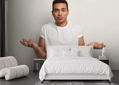 photo of hesitant uncertain hipster guy spreads hands, makes choice, dressed in casual white t shirt Wall mural