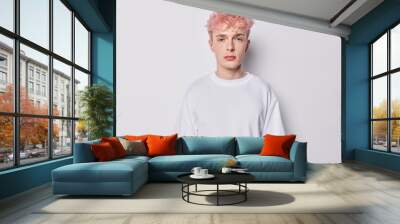 Portrait of attentive hipster guy with pink hair and tattoo on arm dressed in casual basic t shirt looks directly at camera has serious expression isolated over white background belong to subculture Wall mural