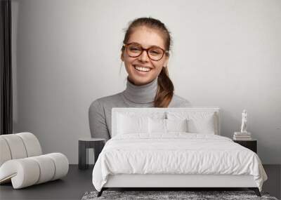 Portrait of beautiful cute teenage girl in good mood wearing her long hair gathered in ponytail laughing, enjoying nice time indoors with friends, posing isolated against blank studio wall background Wall mural