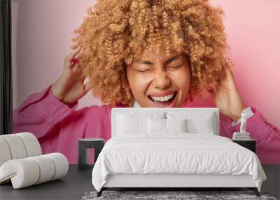 portrait of cheerful woman laughs happily keeps hands on curly hair keeps eyes closed from joy dress Wall mural