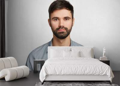 Portrait of confident serious male model has black beard and mustache, dressed in casual denim shirt, looks seriously into camera, isolated over white background. Hipster guy models in white studio Wall mural