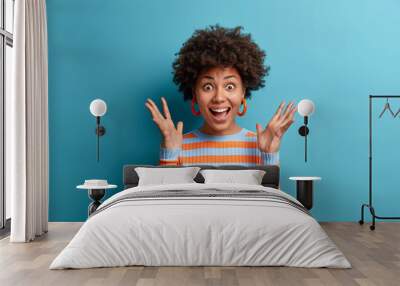 portrait of delighted cheerful ethnic woman reacts on awesome gift, raises palms and stares with eye Wall mural