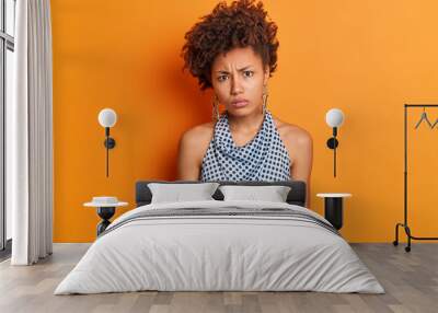 Portrait of displeased offended dark skinned woman looks with disappointed expression wears earrings and fashionable polka dot blouse isolated over orange background. Negative emotions and feelings Wall mural