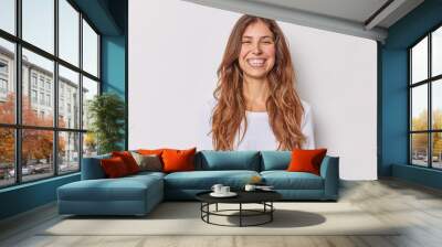 Portrait of good looking European woman smiles broadly with perfect even teeth has long wavy hair dressed in casual jumper isolated over white studio background. Authentic human emotions concept. Wall mural