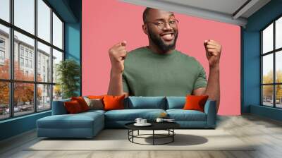 Portrait of successful dark skinned African American male enterpreneur clenches fists with happiness, celebrates his victory, has broad positive smile on face, isolated over pink background. Wall mural