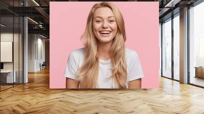 Portrait of young blonde positive female with cheerful expression, dressed in casual white t shirt, rejoices to recieve good job offer, isolated over pink background. Beautiful woman indoor. Wall mural