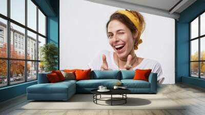 Positive cheerful young woman wearing yellow scarf on head and white casual T-shirt blinking her eyes and smiling pointing at camera with index fingers. Happy attractive woman pointing at you Wall mural