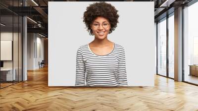 Positive emotions concept. Happy young smiling African American female in spectacles, rejoices unforgettable party with friend, dressed in casual striped jacket, isolated on white background Wall mural