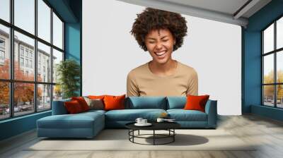 Positive human emotions concept. Happy curly young African American woman with glad expression, giggles and laughs at something funny, squints face from happiness, isolated over white background Wall mural