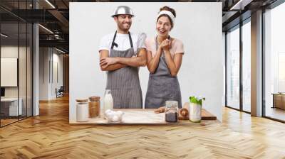 Pretty female cooker wears apron and scarf on head, has glad expression as being promoted to chef, stands at kitchen with male colleague who congratulates her with new position in restaurant Wall mural