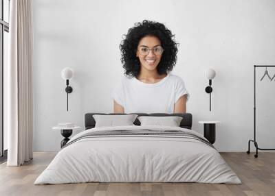 Relaxed carefree smiling young woman wearing white t-shirt and glasses having positive cheerful expression on her face, rejoicing at her leisure time, spending day at home. Horizontal studio shot Wall mural