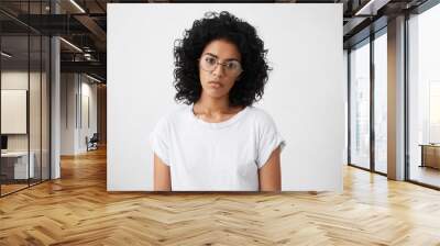 Serious and sad black woman with Afro haircut wearing big elegant glasses and casual clothes posing in studio over white background having thoughtful expression. People, lifestyle, emotions concept Wall mural