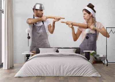 Serious cook competitors pretend that rolling pin is gun, look at each other as on shooting mark, try to prove rightness or case, stand at kitchen table with ingredients and hand made pastry Wall mural