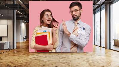 Serious male tutor has lesson with trainee who flirts and expresses symathy, shows stop gesture, refuses to start relationships. Positive young female holds papers, feels love to young teacher Wall mural