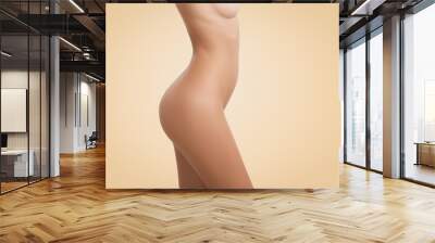 Side cropped view of young female body with naked torso posing isolated against blank wall background with copy space for your text or advertising concept. Portrait of woman with perfect tanned skin Wall mural