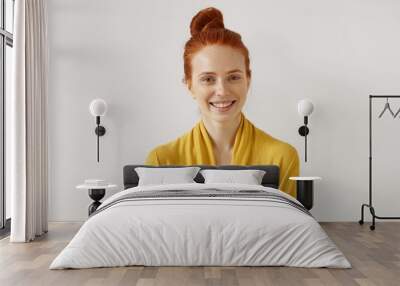 Studio shot of amazing gorgeous young red-haired European female model with healthy freckled skin and no make up posing at white wall, grinning broadly, having happy expression on her pretty face Wall mural