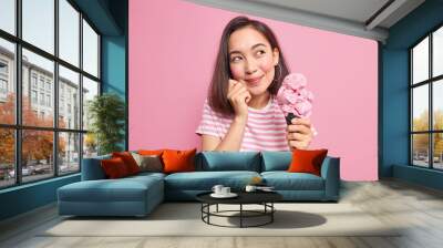 studio shot of dreamy brunette young asian woman with short dark hair looks away eats delicious ice  Wall mural