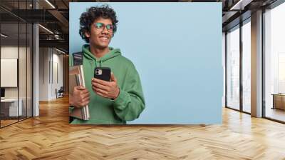 Studio waist up of young smiling delighted Hindu male student standing on left isolated on blue background looking at blank space for your advertisement reading message with good news about his study Wall mural