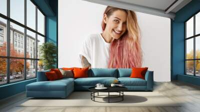 Style, fashion and hair coloring concept. Portrait of gorgeous young female with charming smile, tattoo on arm and long loose hair dyed pink looking at camera, having joyful carefree expression Wall mural