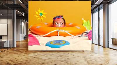 Summer vacation and holiday resort concept. Pensive young woman with goggles on forehead, looks aside thoughtfully, enjoys sun, applies sunscreen on face, poses at sandy beach with different items Wall mural