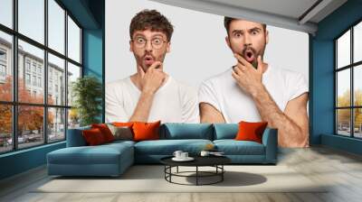 Suprised male corporate workers have stunned expressions, hold chins and stare with bugged eyes, shocked to recieve failure, dressed in casual white t shirts, pose in studio. Team work concept Wall mural